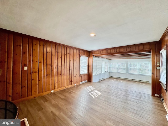 spare room featuring light wood finished floors, baseboard heating, a healthy amount of sunlight, and wood walls