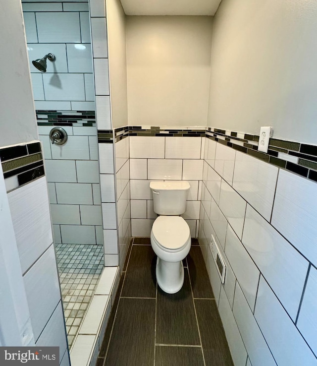 bathroom featuring toilet, tile walls, wainscoting, and a shower stall