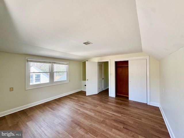 unfurnished bedroom featuring visible vents, two closets, wood finished floors, baseboards, and vaulted ceiling