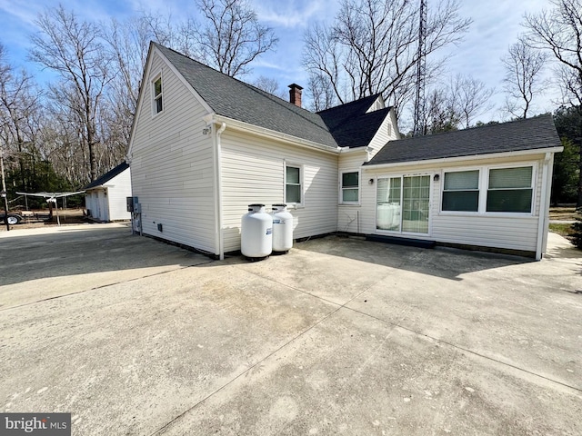 rear view of house featuring a shingled roof and a chimney