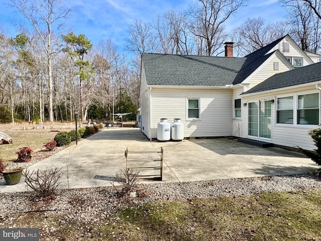 rear view of property featuring a shingled roof, a patio, and a chimney