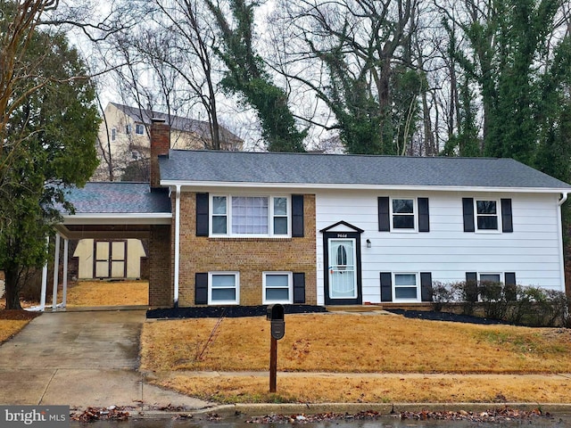 raised ranch featuring brick siding, concrete driveway, a carport, a chimney, and a front yard