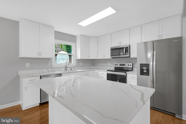 kitchen featuring stainless steel appliances, light stone counters, a sink, and white cabinets