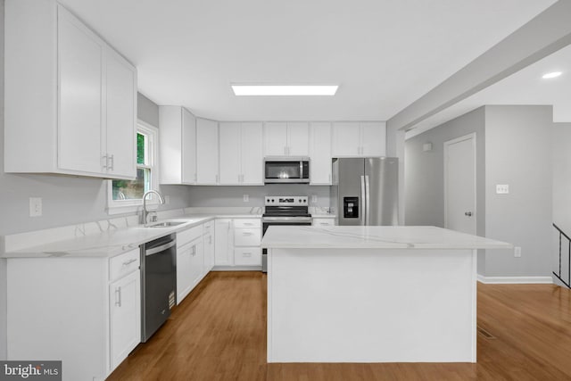 kitchen featuring stainless steel appliances, a kitchen island, a sink, and white cabinets