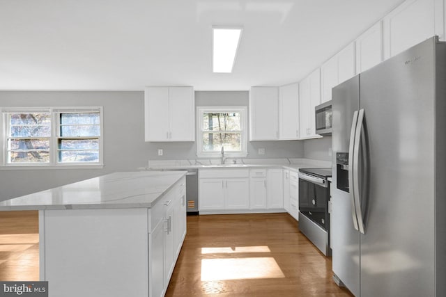 kitchen featuring light stone counters, a center island, light wood-style flooring, appliances with stainless steel finishes, and white cabinets