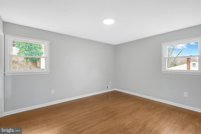 spare room featuring a healthy amount of sunlight, visible vents, baseboards, and wood finished floors