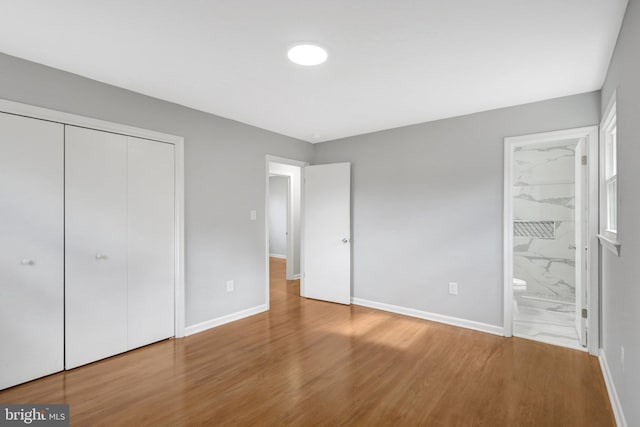 unfurnished bedroom with ensuite bath, a closet, baseboards, and wood finished floors