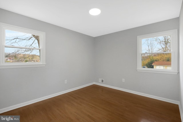 unfurnished room featuring visible vents, baseboards, and dark wood-type flooring