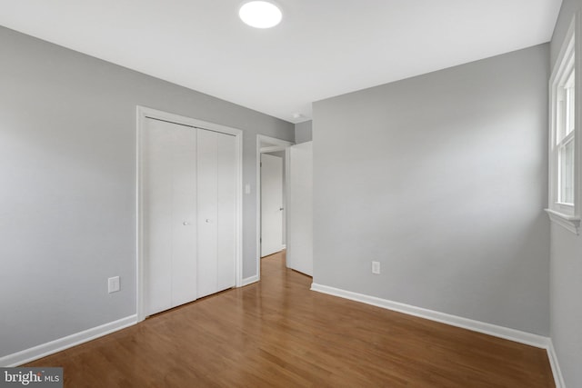 unfurnished bedroom with a closet, wood finished floors, and baseboards