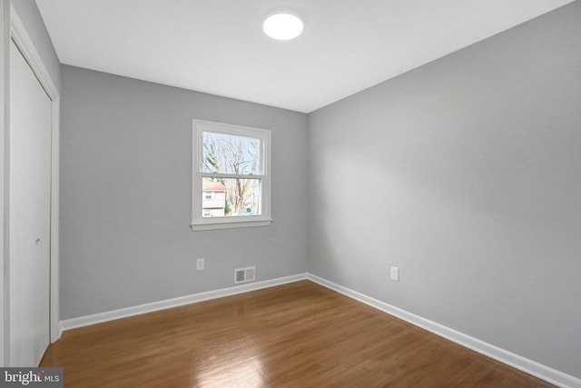 unfurnished bedroom with a closet, visible vents, baseboards, and wood finished floors