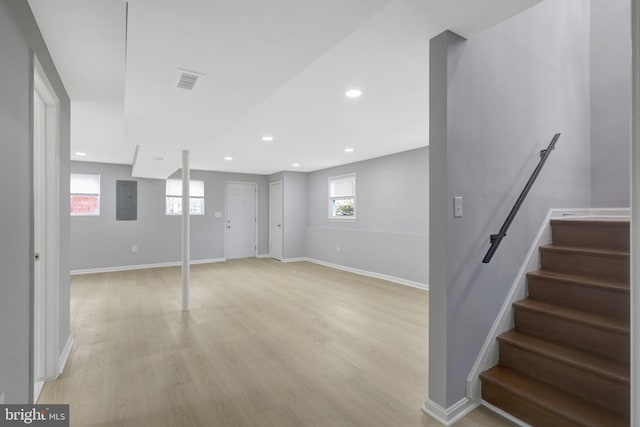 below grade area featuring light wood-style flooring, visible vents, baseboards, stairs, and electric panel