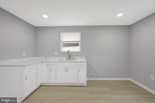 kitchen with light wood-style flooring, baseboards, white cabinets, and a sink