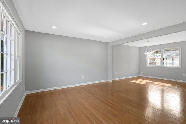 spare room featuring recessed lighting, a notable chandelier, baseboards, and wood finished floors