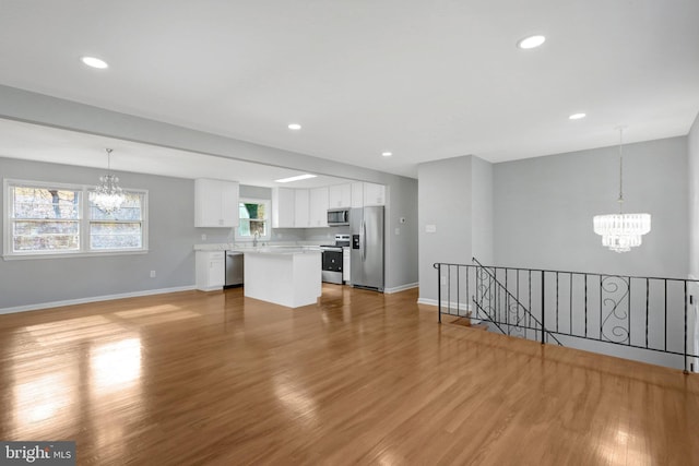 unfurnished living room with light wood-type flooring, a notable chandelier, baseboards, and recessed lighting