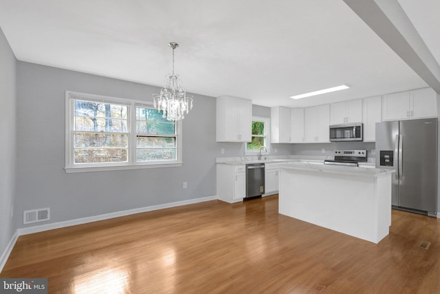 kitchen with stainless steel appliances, light countertops, visible vents, white cabinetry, and wood finished floors