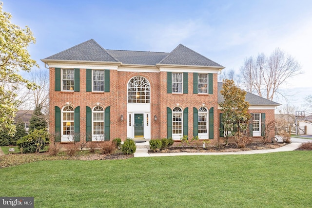 colonial-style house with a shingled roof, brick siding, and a front lawn