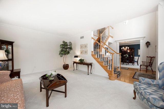 living area featuring crown molding, stairway, carpet, and an inviting chandelier