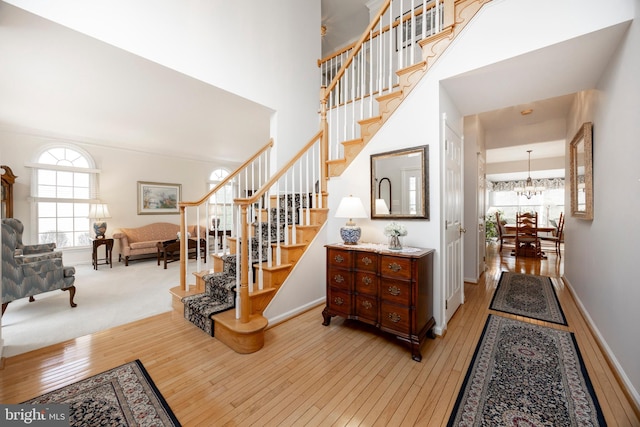 interior space featuring a towering ceiling, stairway, an inviting chandelier, light wood-style floors, and baseboards