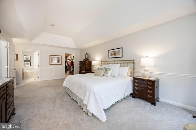 bedroom featuring a closet, a raised ceiling, light colored carpet, a spacious closet, and ensuite bath