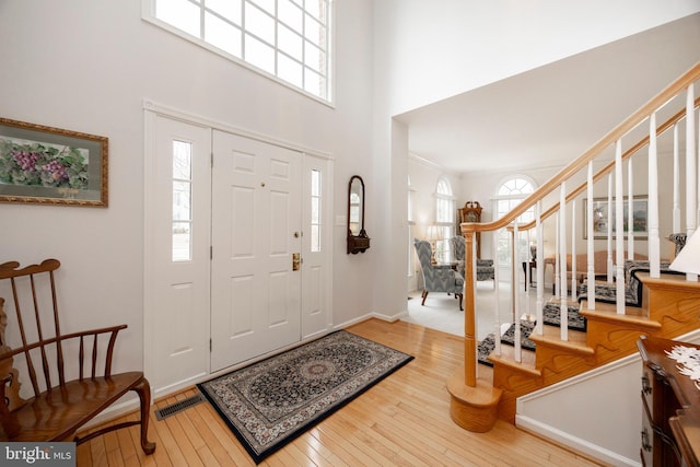 entryway featuring visible vents, hardwood / wood-style floors, a high ceiling, baseboards, and stairs