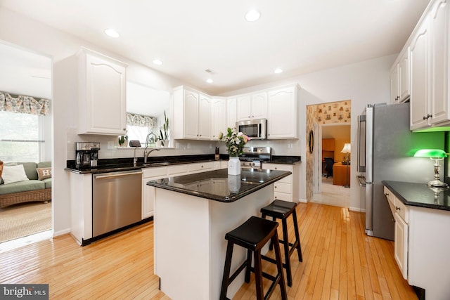 kitchen featuring a breakfast bar, stainless steel appliances, light wood-style flooring, white cabinetry, and a kitchen island