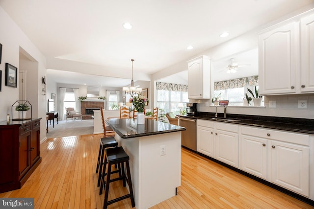 kitchen with light wood-style floors, white cabinetry, a kitchen island, a sink, and dishwasher