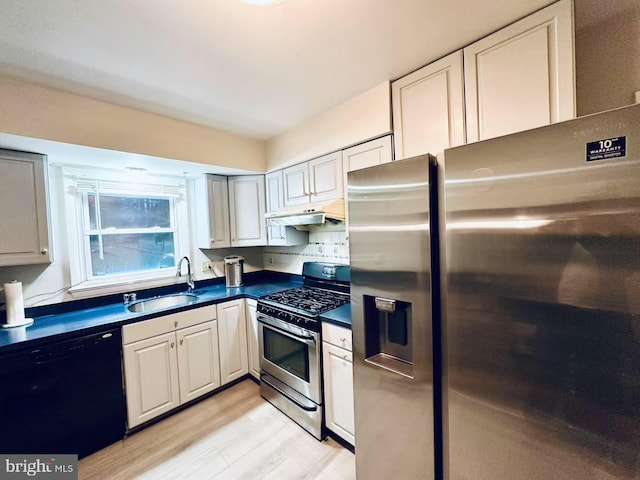 kitchen with light wood-style floors, dark countertops, stainless steel appliances, under cabinet range hood, and a sink