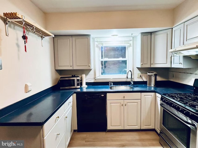 kitchen featuring stainless steel appliances, dark countertops, light wood-style flooring, a sink, and under cabinet range hood