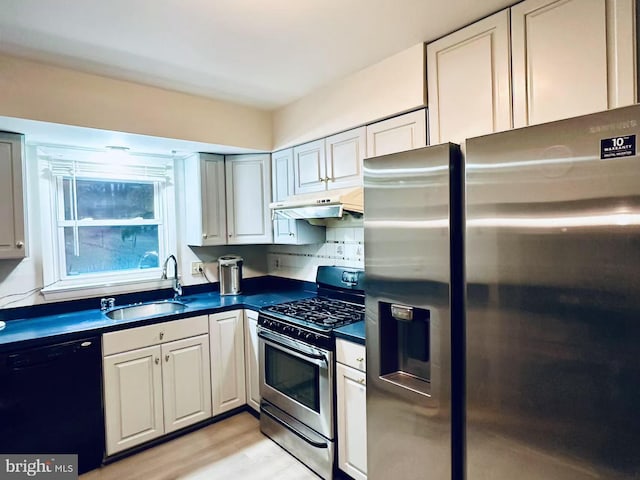 kitchen featuring dark countertops, appliances with stainless steel finishes, a sink, light wood-type flooring, and under cabinet range hood