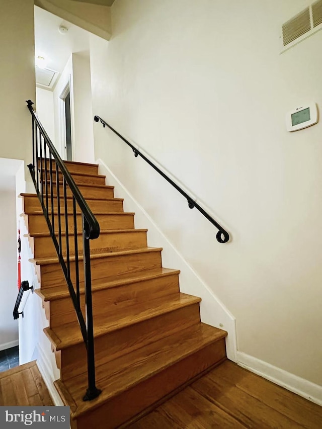 staircase featuring attic access, wood finished floors, visible vents, and baseboards