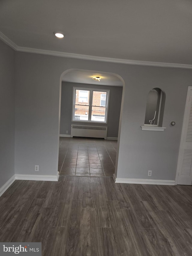 spare room with radiator heating unit, crown molding, wood finished floors, arched walkways, and baseboards