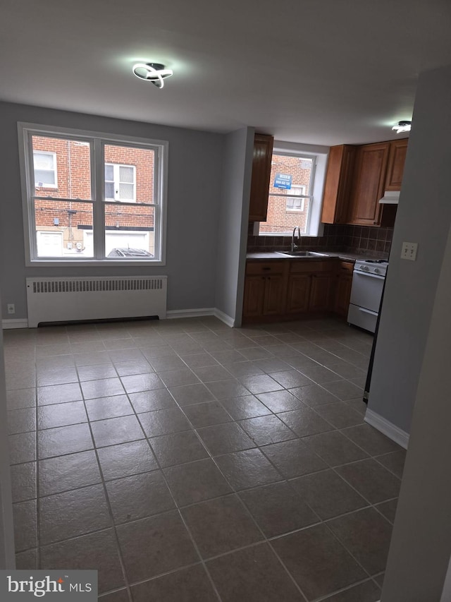 kitchen featuring a sink, tasteful backsplash, radiator heating unit, dark tile patterned floors, and white gas range