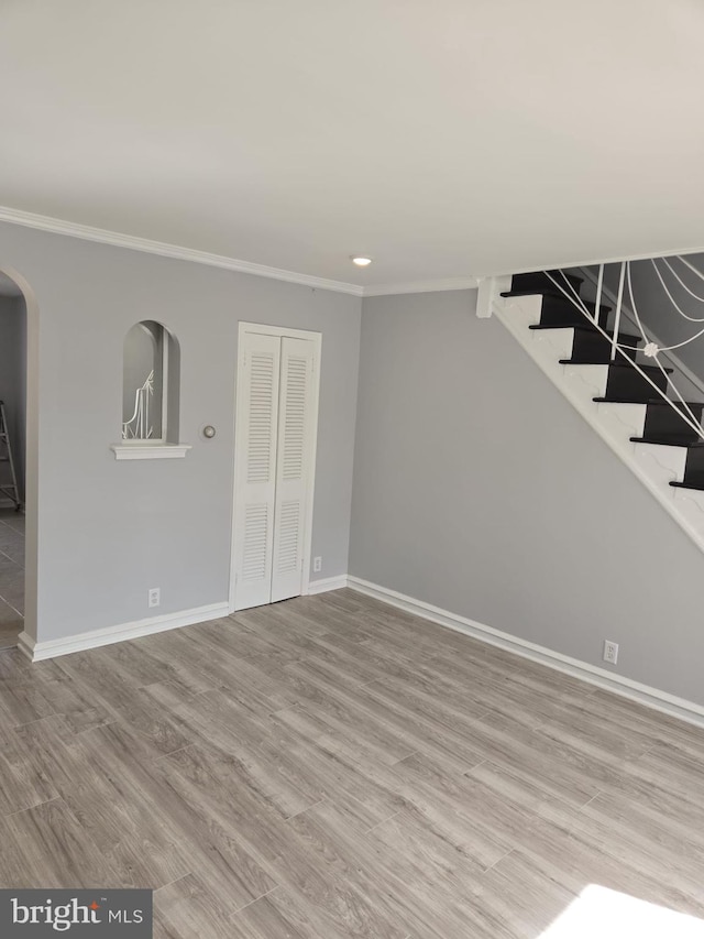 unfurnished living room featuring stairs, ornamental molding, wood finished floors, and baseboards