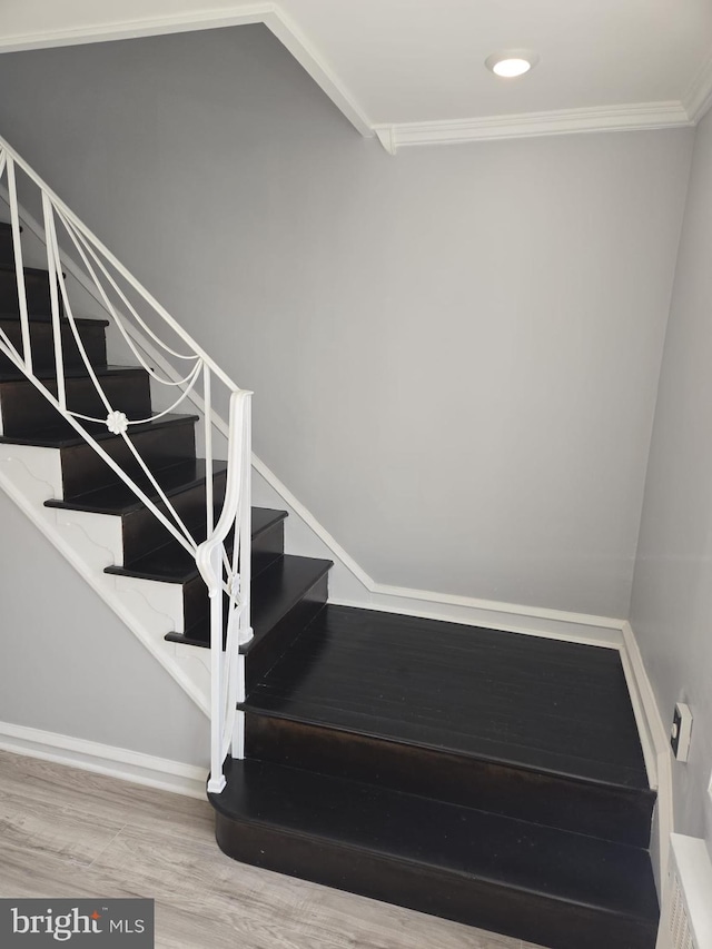 staircase featuring wood finished floors, baseboards, and ornamental molding