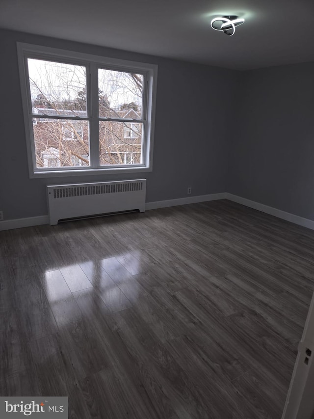 spare room featuring radiator, dark wood-type flooring, and baseboards