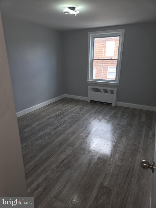 empty room featuring radiator, baseboards, and dark wood-style flooring