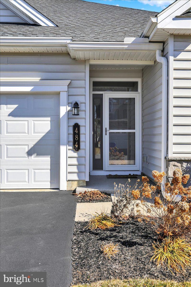 entrance to property with a garage and roof with shingles