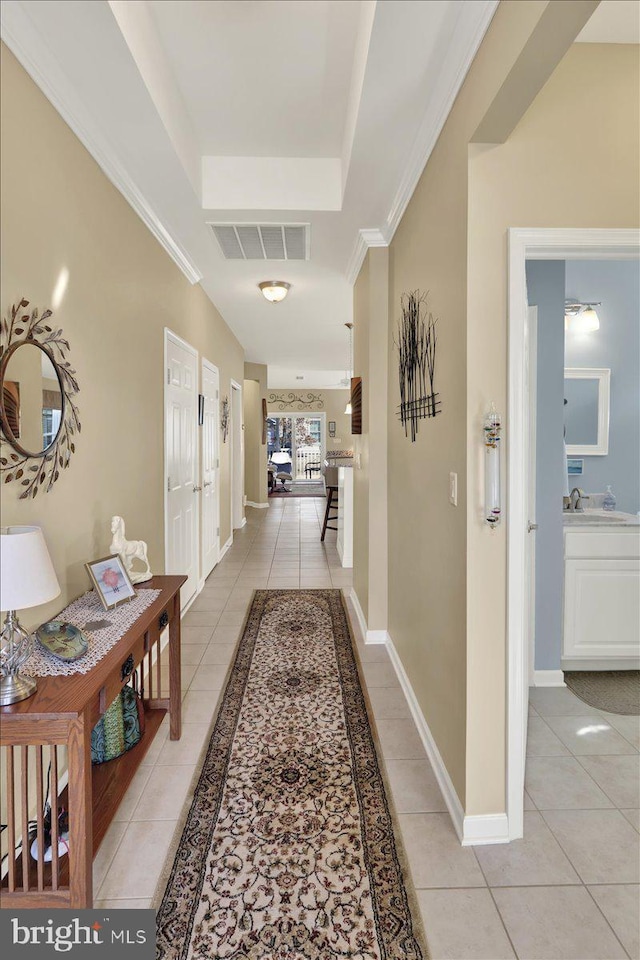 hall with baseboards, visible vents, a tray ceiling, light tile patterned flooring, and crown molding