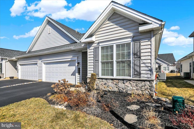 view of front facade with a front lawn, driveway, stone siding, cooling unit, and a garage