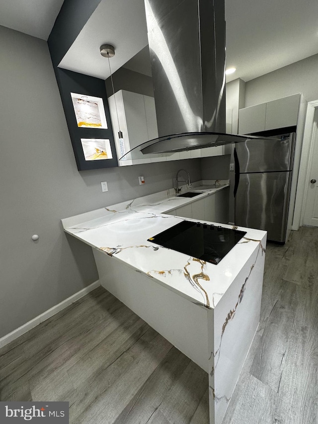 kitchen featuring a sink, light countertops, freestanding refrigerator, light wood finished floors, and island exhaust hood