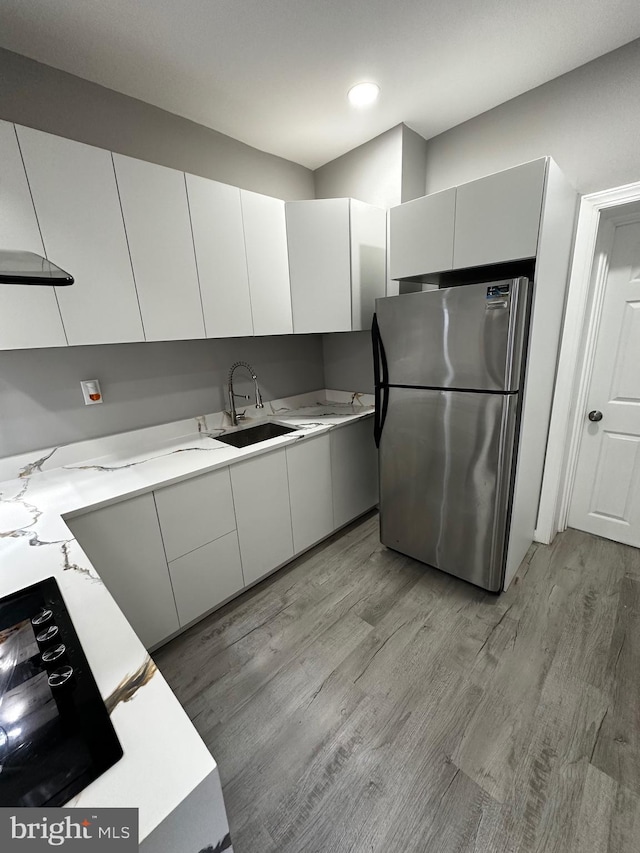 kitchen with freestanding refrigerator, light countertops, a sink, and light wood-style flooring