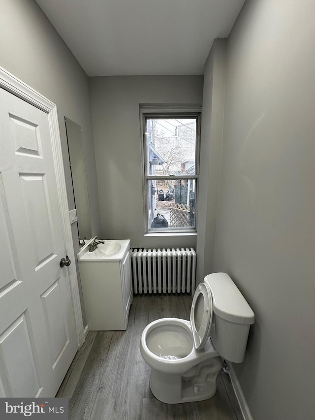 half bath with toilet, wood finished floors, vanity, baseboards, and radiator