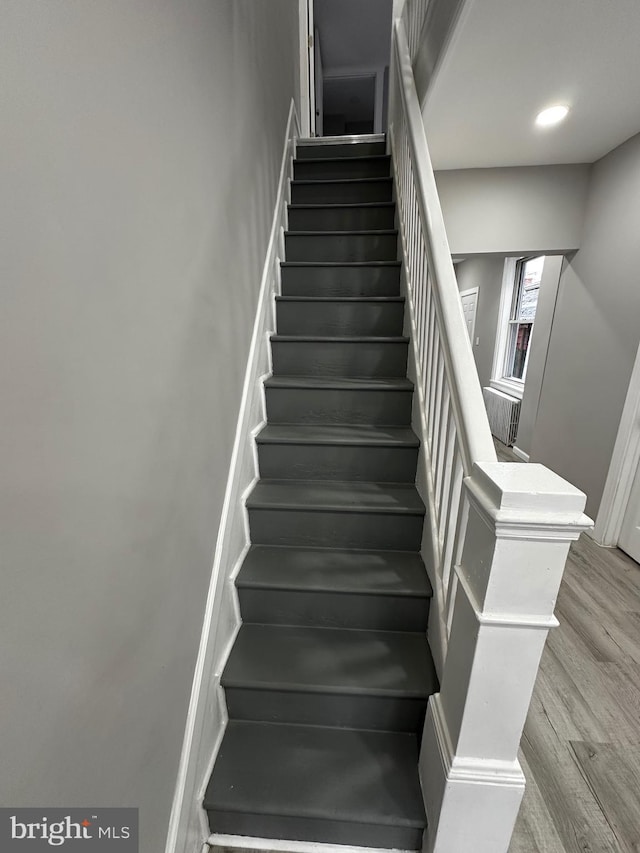 stairs featuring wood finished floors and recessed lighting