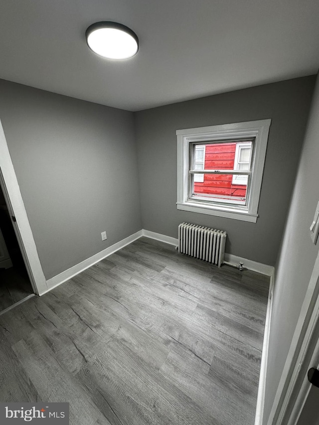 unfurnished room with baseboards, dark wood-style flooring, and radiator