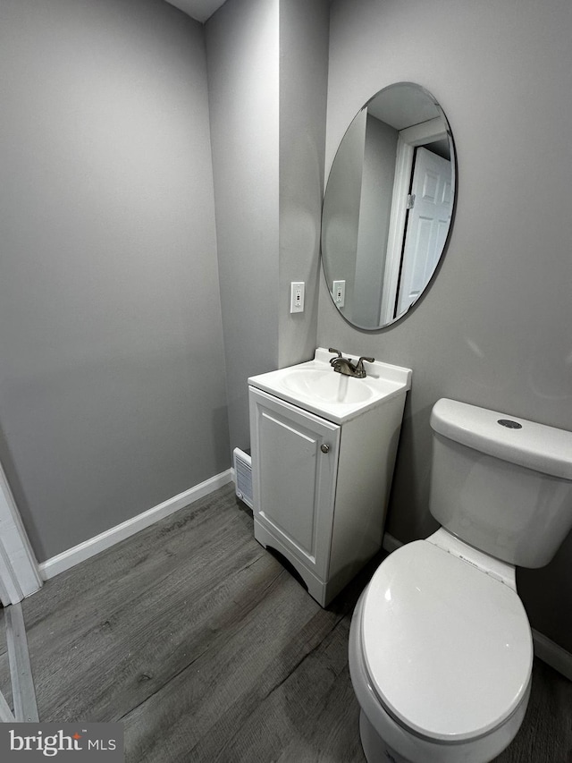 half bath featuring toilet, baseboards, wood finished floors, and vanity