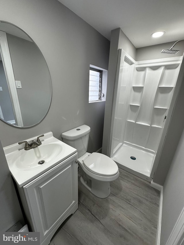 bathroom featuring toilet, a stall shower, wood finished floors, and vanity