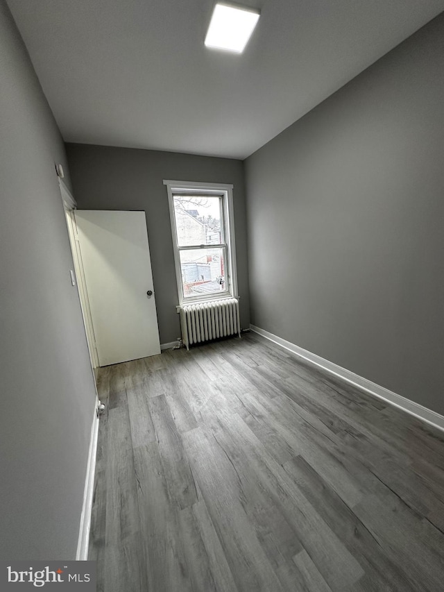 unfurnished room featuring baseboards, radiator heating unit, and wood finished floors