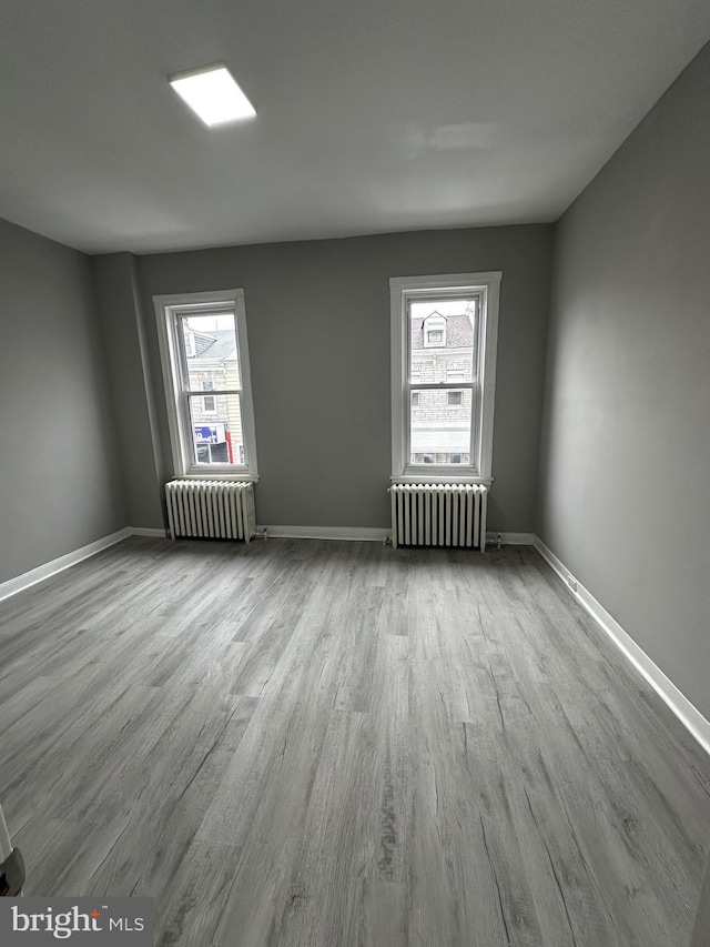 empty room featuring baseboards, radiator heating unit, and wood finished floors