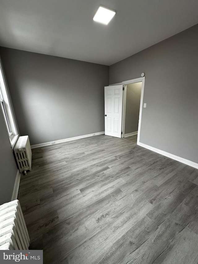 unfurnished bedroom with heating unit, baseboards, and dark wood-style flooring