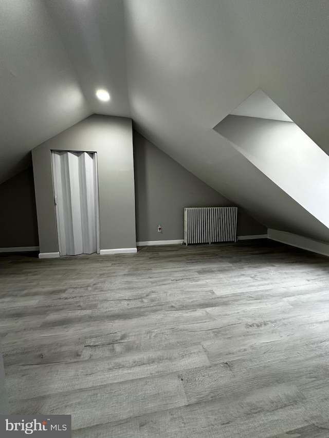 bonus room with radiator, vaulted ceiling, baseboards, and wood finished floors